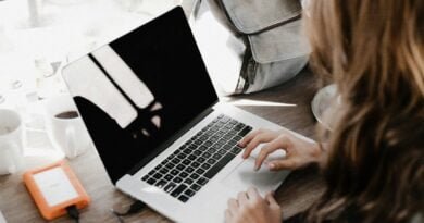 girl wearing grey long-sleeved shirt using MacBook Pro on brown wooden table