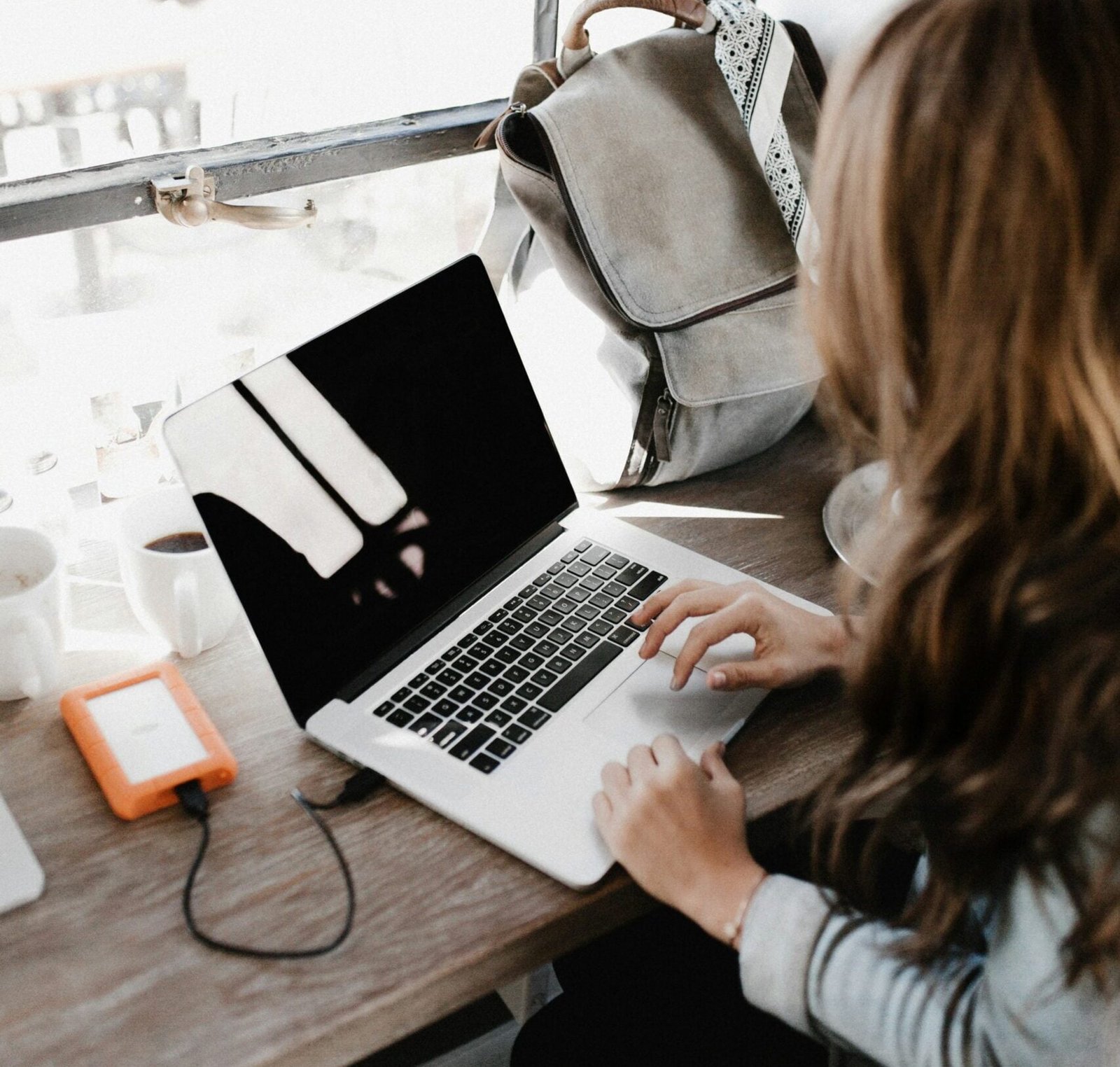 girl wearing grey long-sleeved shirt using MacBook Pro on brown wooden table